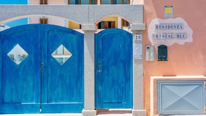 A building with two large blue doors, a sign reading "RESIDENZA CRISTAL BLU", and a small window with a view of the interior. - Residence con piscina a 300 mt dal mare (Santa Teresa di Gallura)