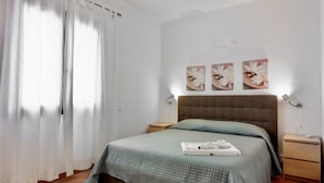 A neatly made bed with a green quilt, a bedside table with a lamp, and a wall with three floral paintings. - Residence con piscina a 300 mt dal mare (Santa Teresa di Gallura)