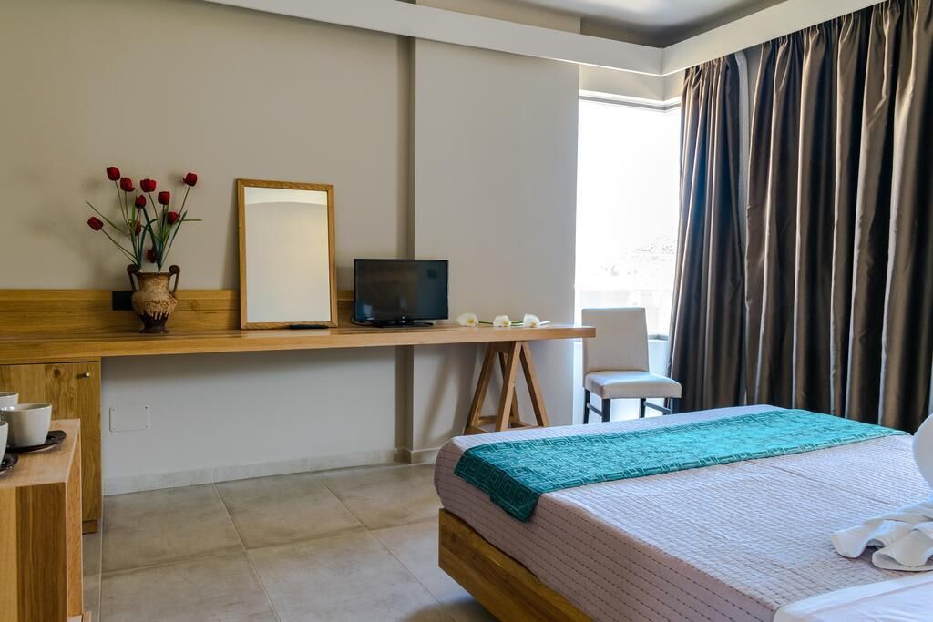 A hotel room with a bed, a desk with a computer, a chair, and a window with curtains.