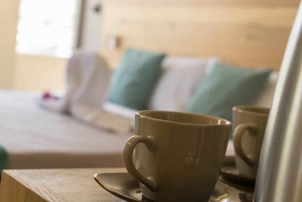 Una mesa de madera con una taza y plato, una cama con almohadas y una ventana al fondo.