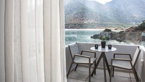Varanda com mesa e cadeiras, vista para paisagem costeira com montanhas.