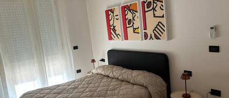 A bedroom with a bed, a bedside table, a lamp, and a wall-mounted air conditioner.