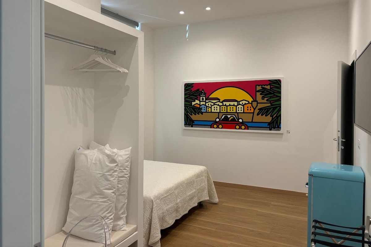 A room with a bed, a wardrobe, a painting, and a vintage-style refrigerator.