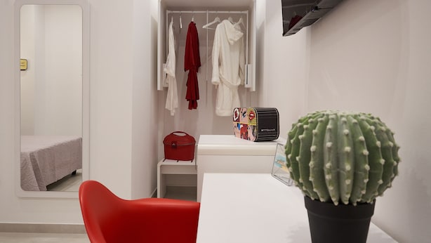 A modern room with a bed, a red chair, a closet with hanging clothes, a small table with a cactus, and a red bag. - Glave Rooms (Termoli)