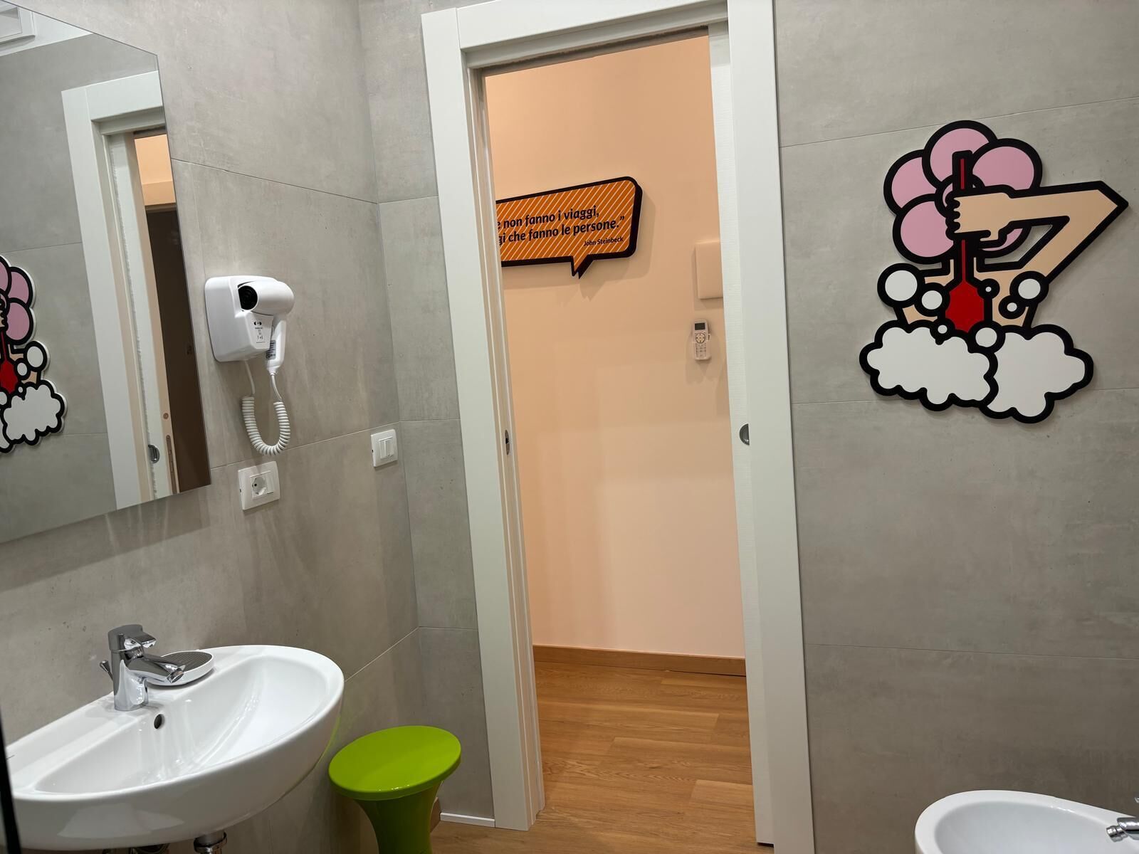 A bathroom with a white sink, a green trash bin, a hairdryer, and a wall-mounted phone.