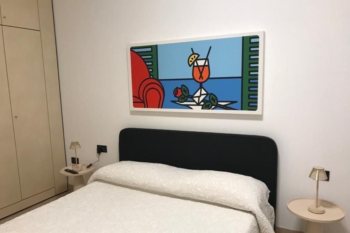 A hotel room with a bed, a nightstand, a lamp, and a wall-mounted painting.