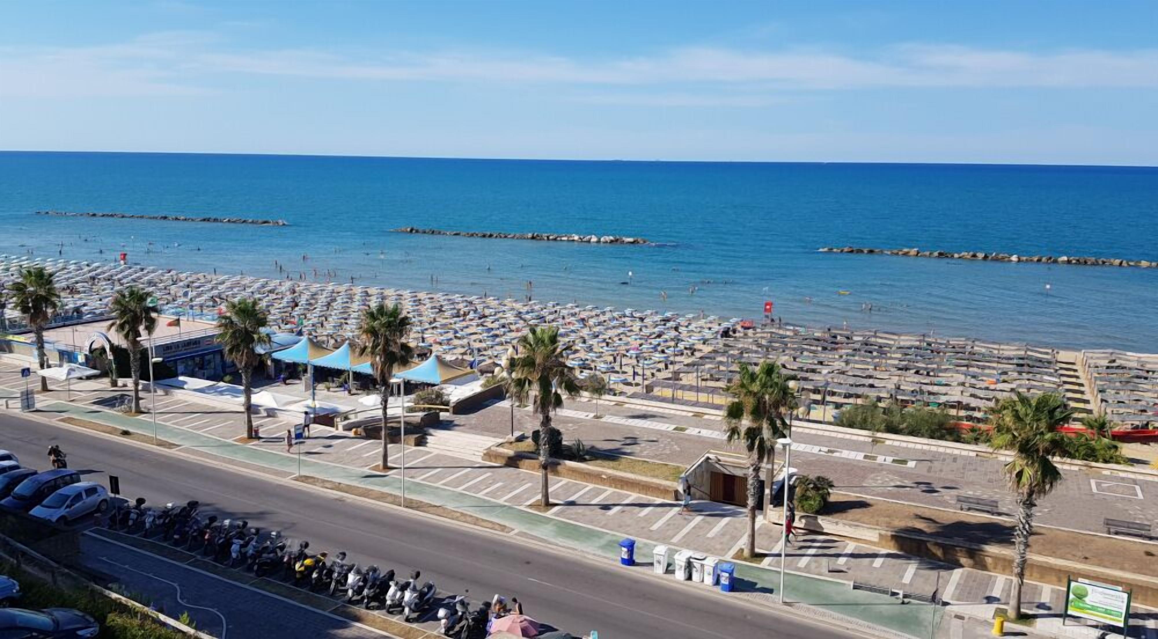 A coastal area with a beach, parked cars, and a road.
