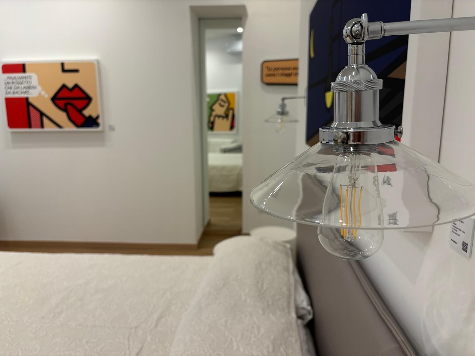 A room with a bed, a wall-mounted lamp, and a painting.