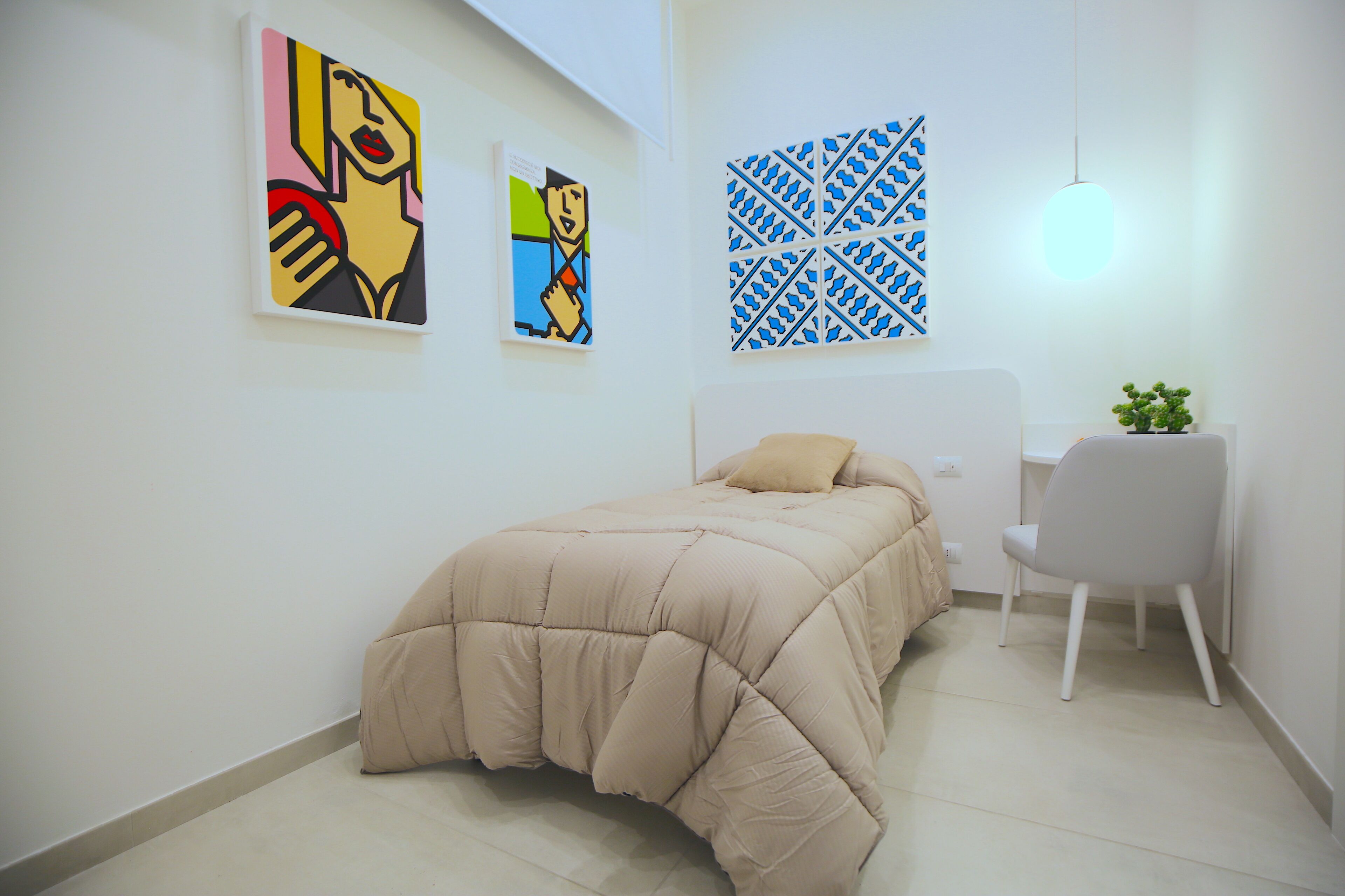 A bedroom with a bed, a chair, and two artworks on the wall.