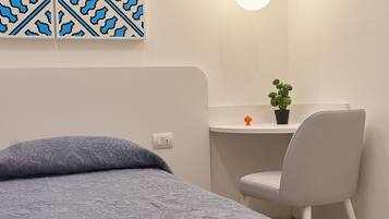 A bedroom with a bed, a desk with a chair, a hanging light, and a wall decoration.