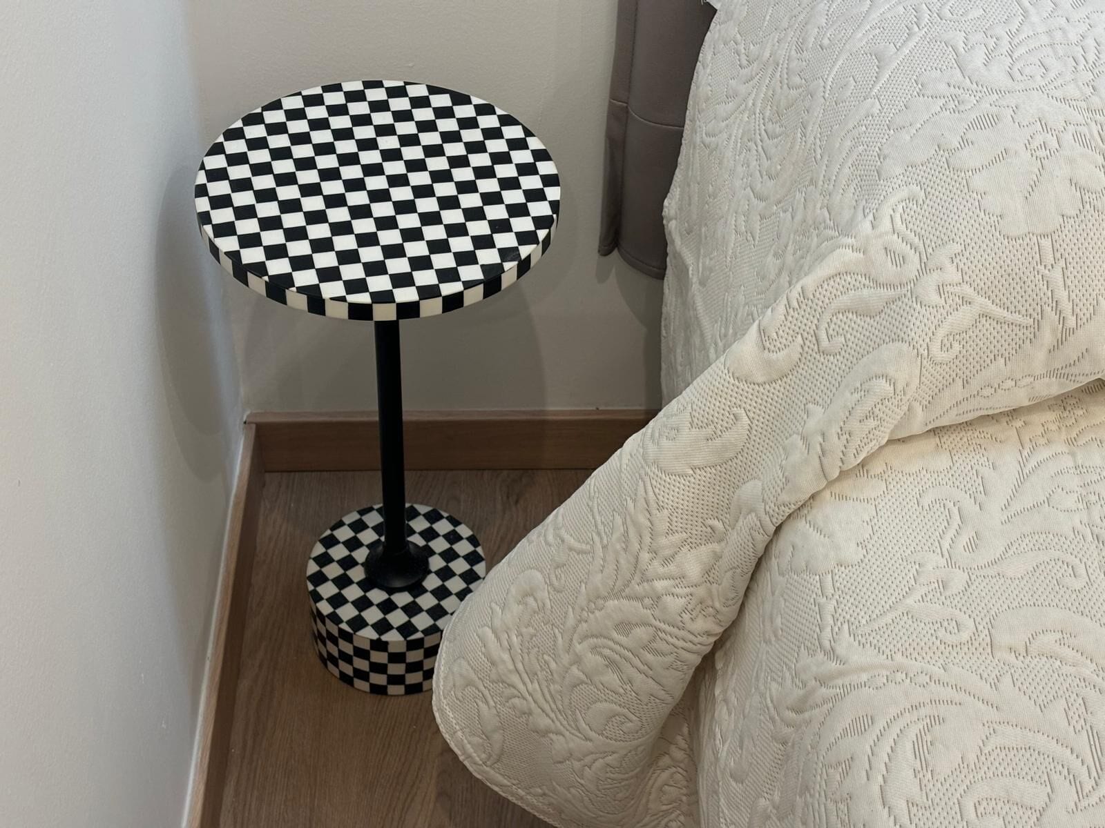 Una mesa redonda con cubierta a cuadros blancos y negros y base a juego, ubicada junto a un tejido blanco con textura.