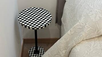 Una mesa redonda con cubierta a cuadros blancos y negros y base a juego, ubicada junto a un tejido blanco con textura.