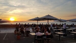 An outdoor dining area with tables and chairs, umbrellas, and a view of the sunset over the water. - Glave Rooms (Termoli)
