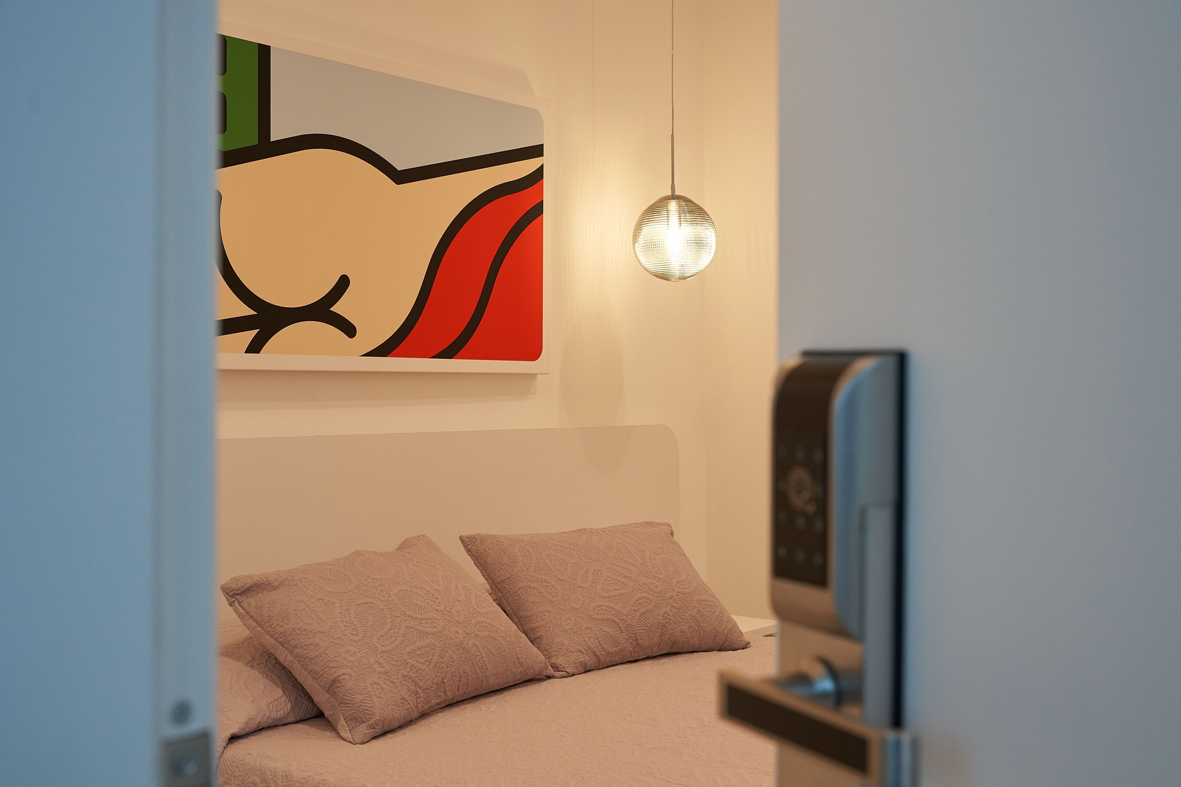 A modern bedroom with a bed, pillows, a wall-mounted artwork, and a pendant light.