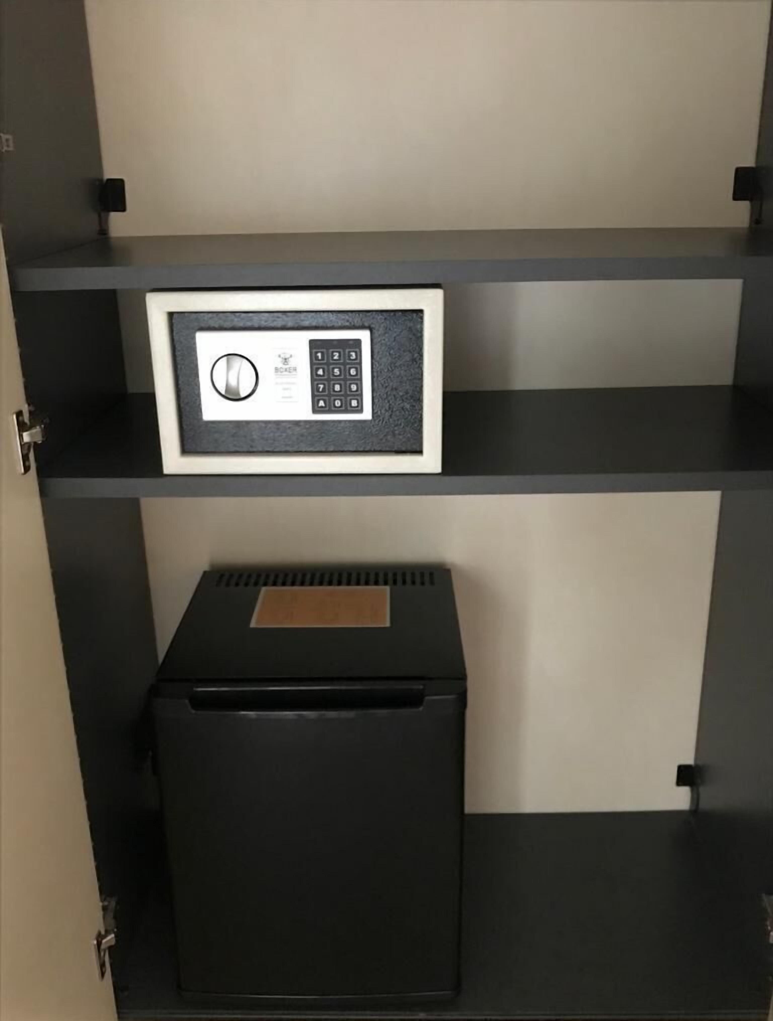 A safe deposit box with a keypad and a small metal plate on top, located in a black metal cabinet with shelves.
