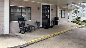 A covered outdoor area with a bench, a door, and a trash can. - Studio 6 Millington, Tn (Millington)