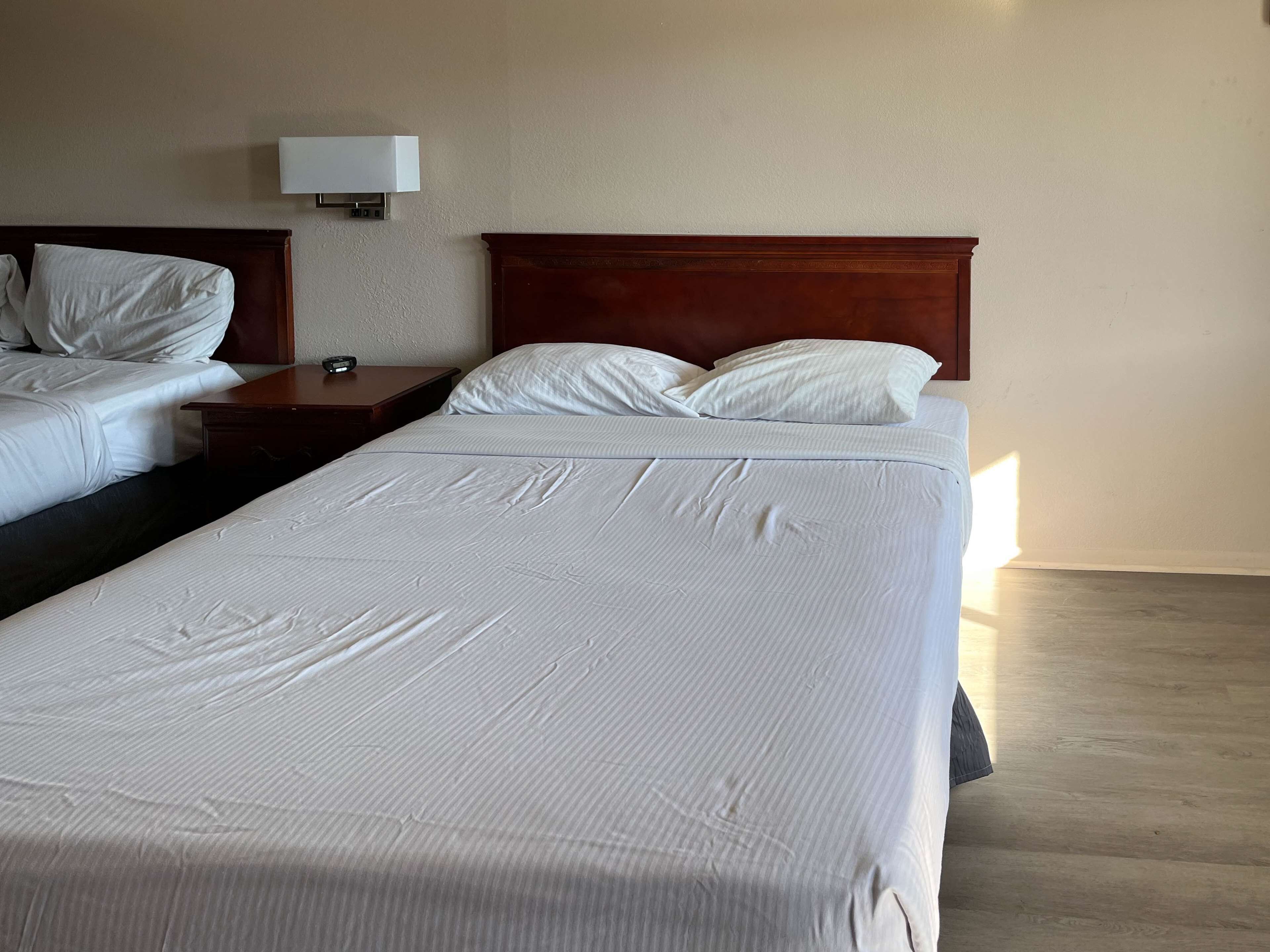A hotel room with two beds, a bedside table with a lamp, and a wooden headboard.