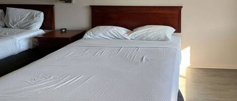 Quarto de hotel com duas camas, uma mesa de cabeceira com abajur e uma cabeceira de madeira.
