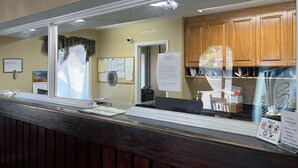 A hotel reception area with a wooden counter, a bulletin board with notices, and a view of the hotel's interior through a window. - Studio 6 Millington, Tn (Millington)