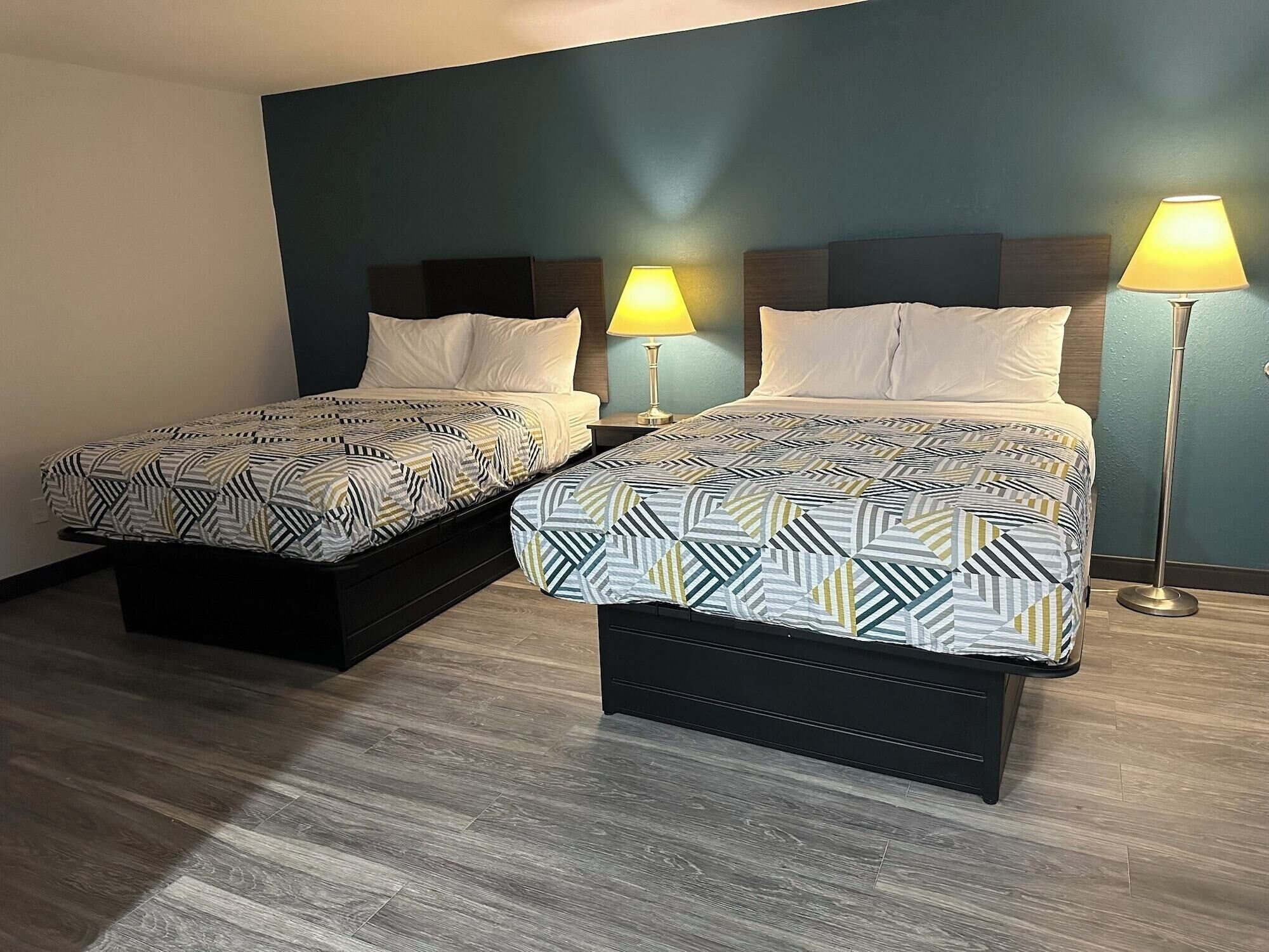 Een hotelkamer met twee bedden, elk met een beddekleed en kussens met een patroon, een nachtkastje met een lamp, en een vloerlamp.