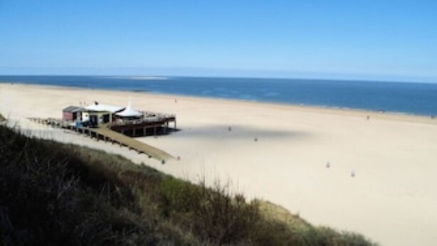 Ein Strand mit einem kleinen Gebäude, vermutlich eine Strandhütte oder ein Kiosk, direkt am Wasser.