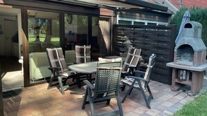 Eine Terrasse im Freien mit Tisch und Stühlen, einem Backsteinboden, einer Glastür zum Verschieben und einem Steinofen.