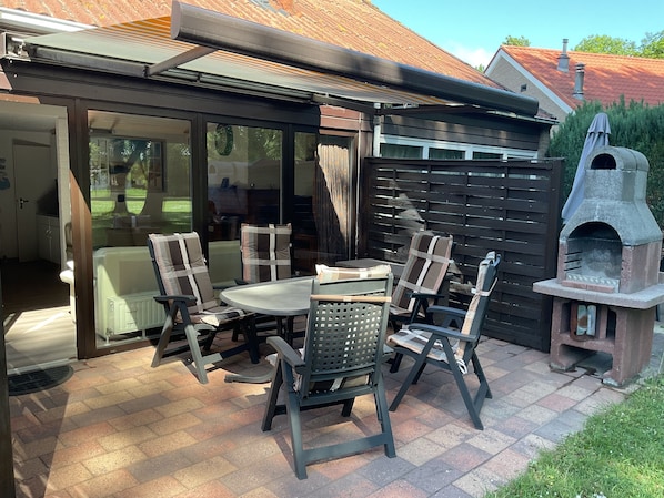 An outdoor patio with a table and chairs, a brick floor, a sliding glass door, and a stone oven.