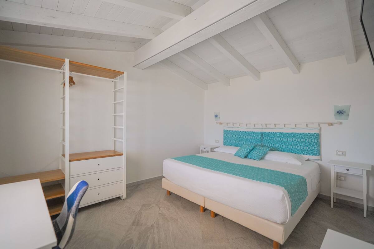 Un dormitorio con cama, armario con estante integrado, escritorio y silla.