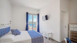 Un dormitorio con una cama, un televisor montado en la pared, una mesita blanca y una silla.