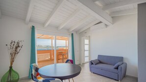 Un salón moderno con una mesa redonda, sillas coloridas, un sofá azul y vistas a una terraza exterior a través de un ventanal.