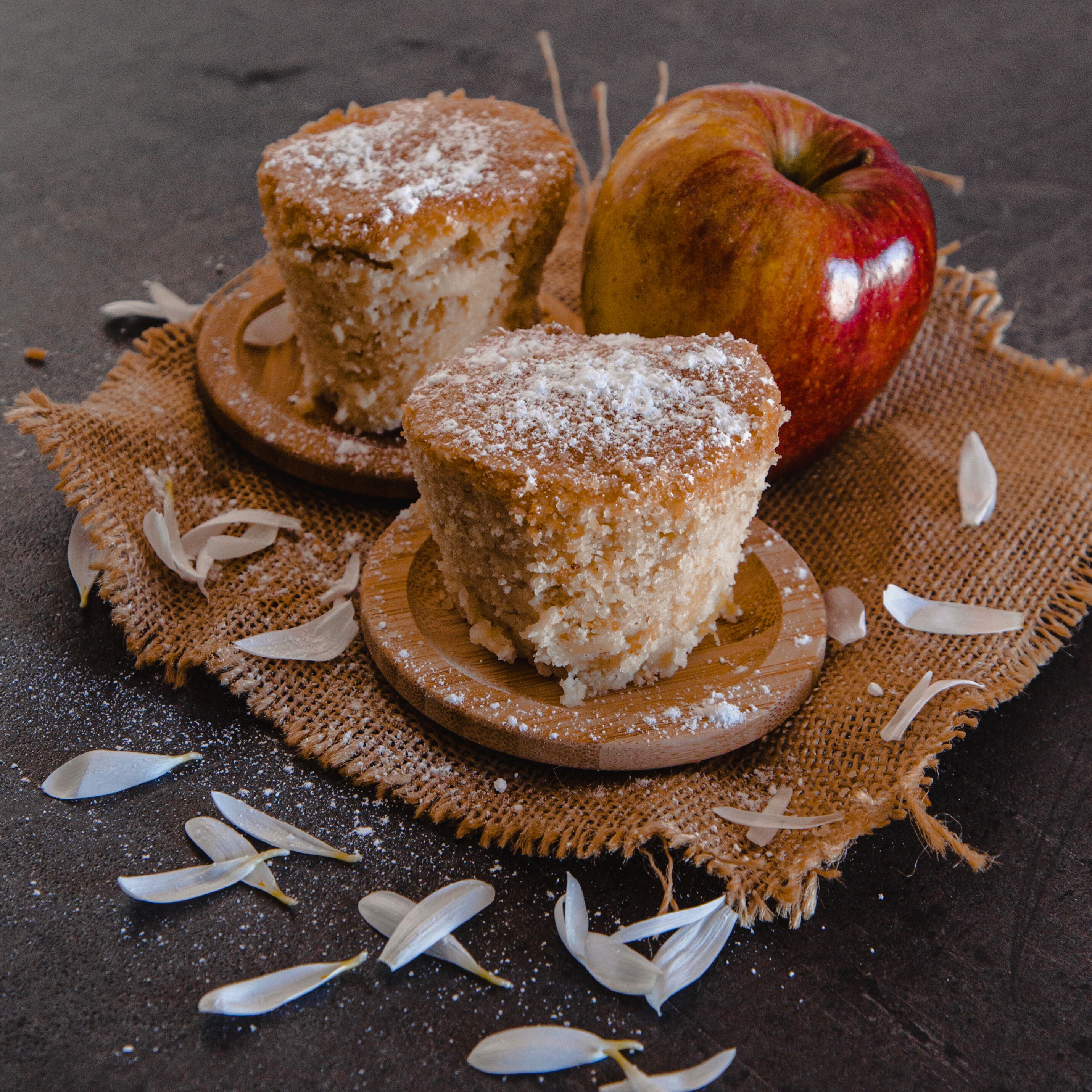 Two muffins on wooden coasters with an apple and scattered almond slices on a burlap cloth.