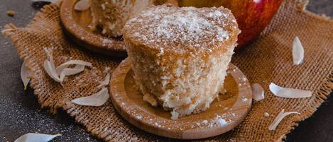 Two muffins on wooden coasters with an apple and scattered almond slices on a burlap cloth.