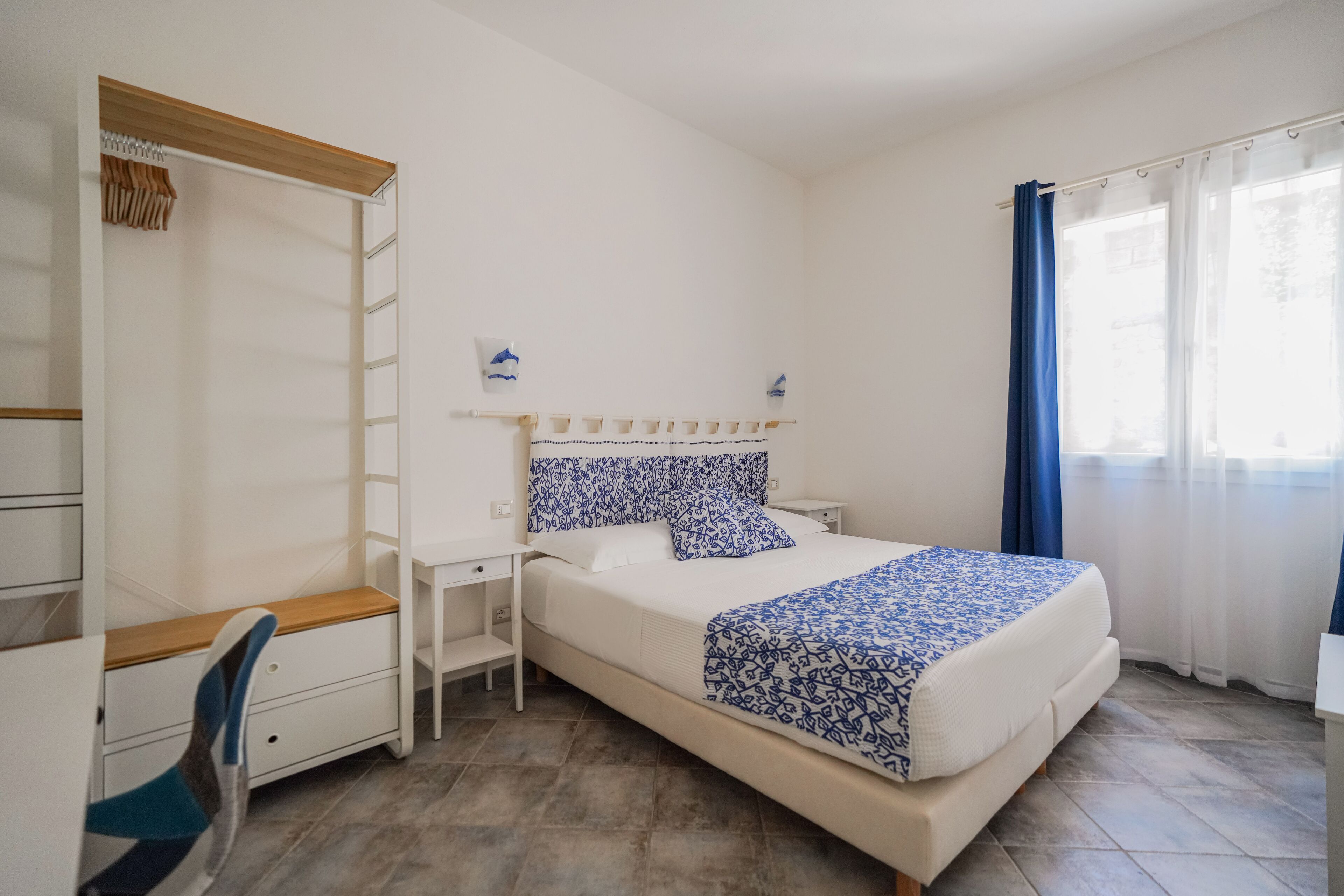 A bedroom with a bed, a desk, a chair, a wardrobe, and a window with curtains.