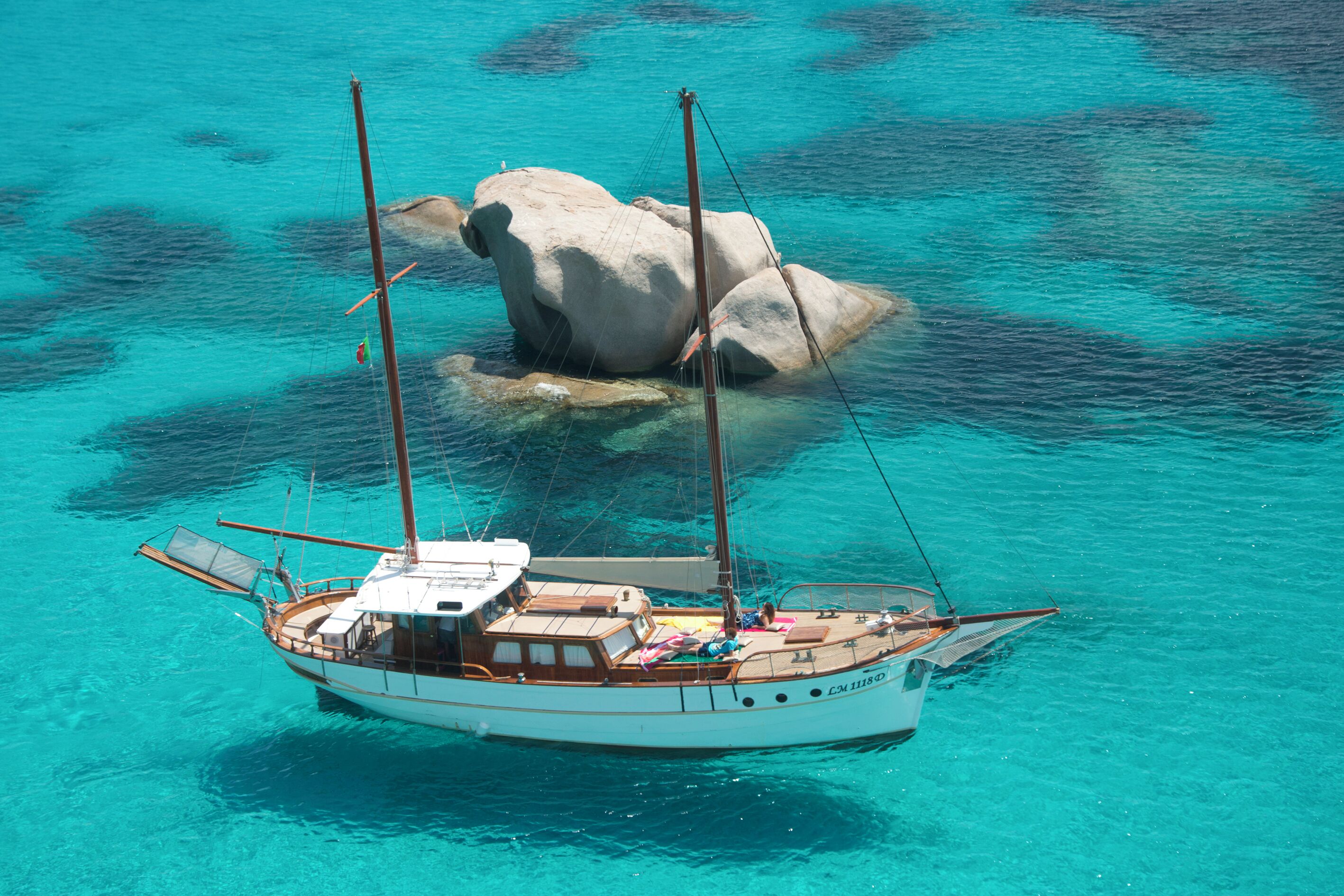 A sailboat anchored near a large rock in clear turquoise waters.