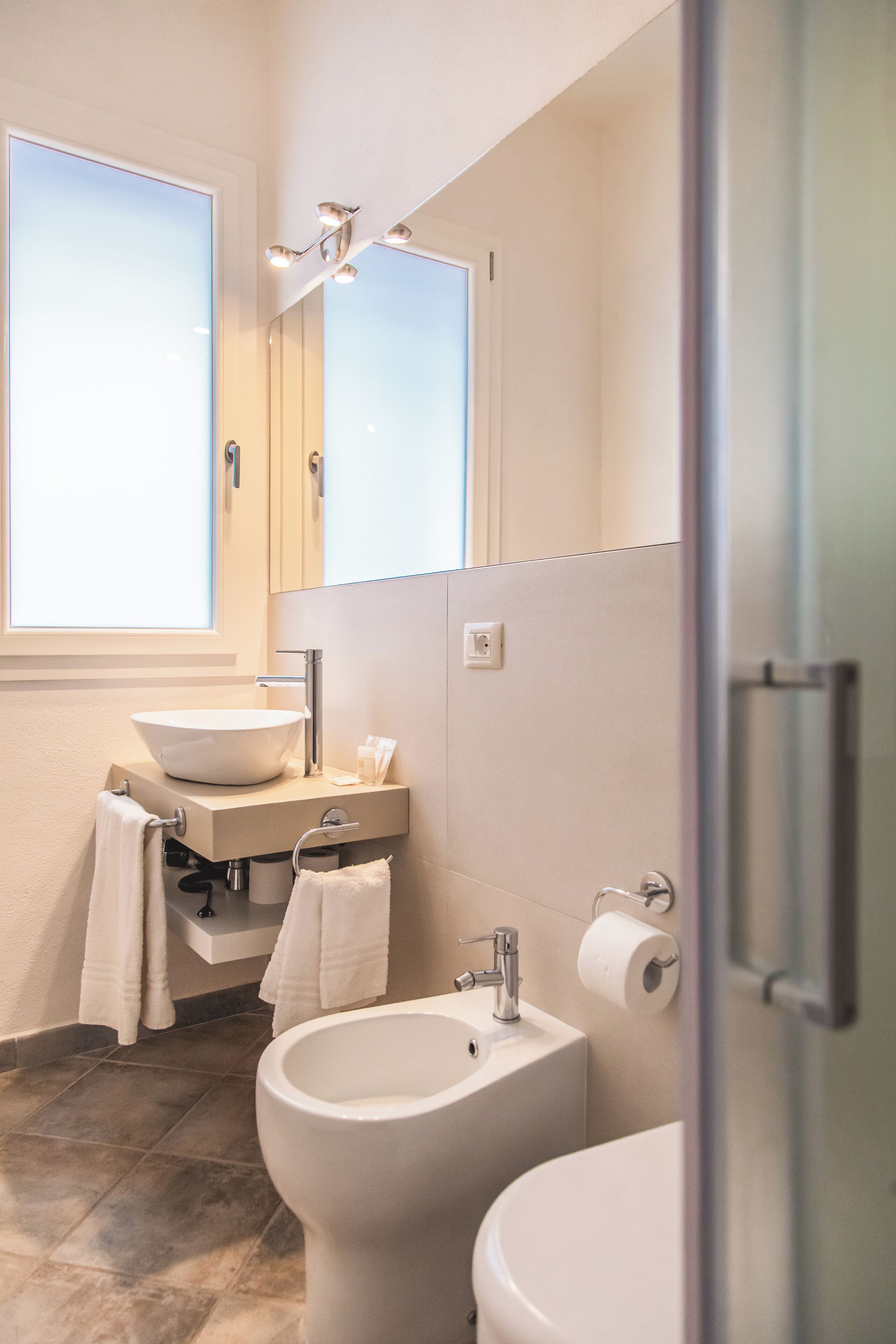 Un baño moderno con un ventanal grande, un lavabo, un inodoro y un espejo.