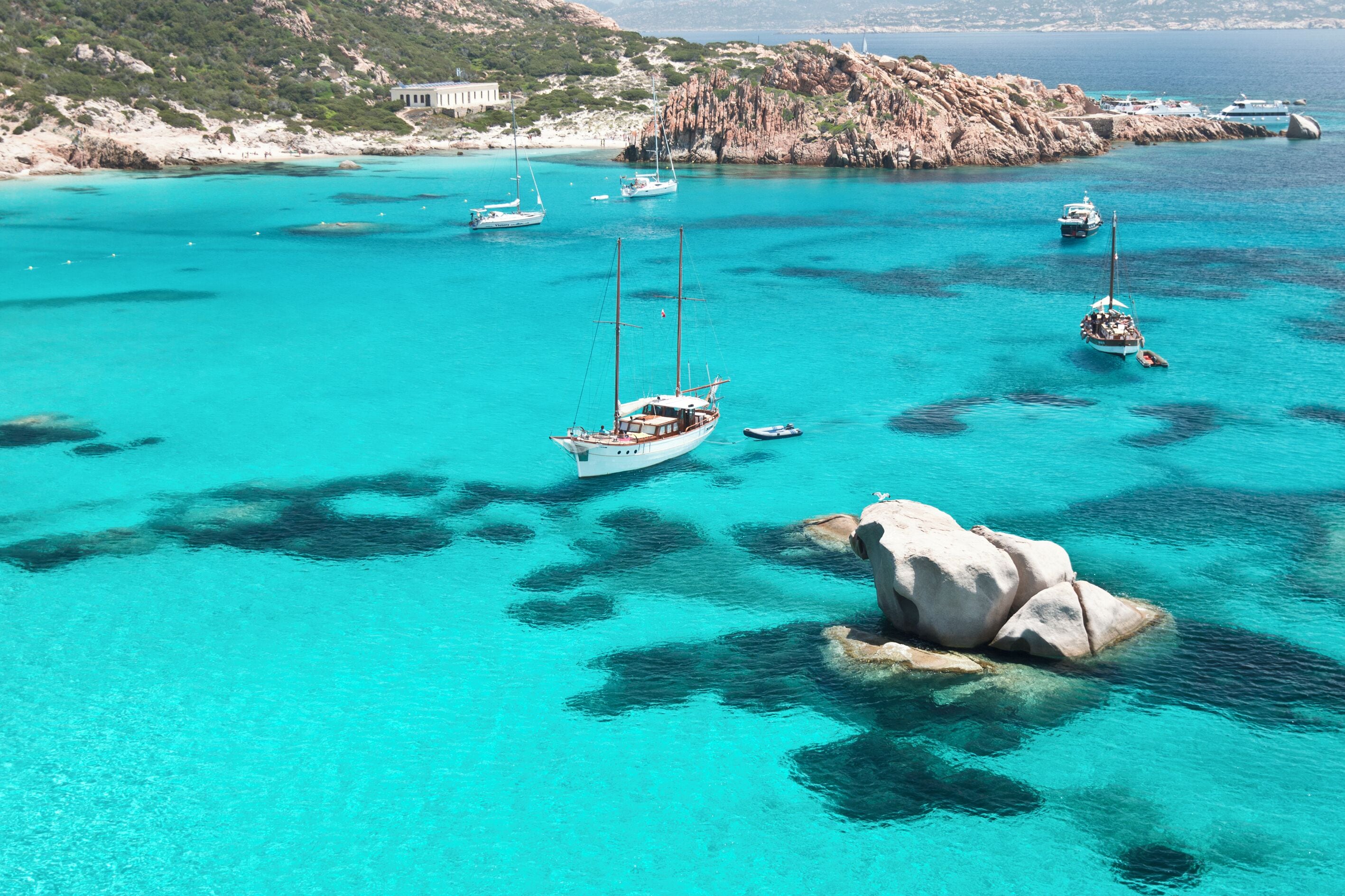 A coastal area with clear turquoise waters, boats, and rocky terrain.