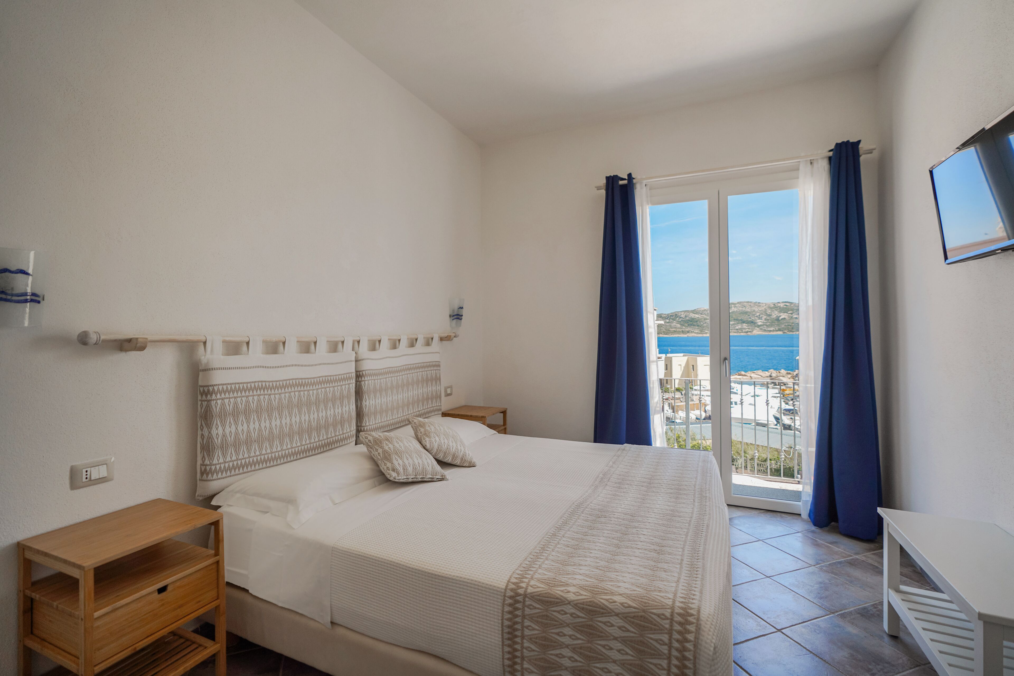 Ein Schlafzimmer mit Bett, Nachttisch, kleinem Tisch und Meerblick vom Balkon.