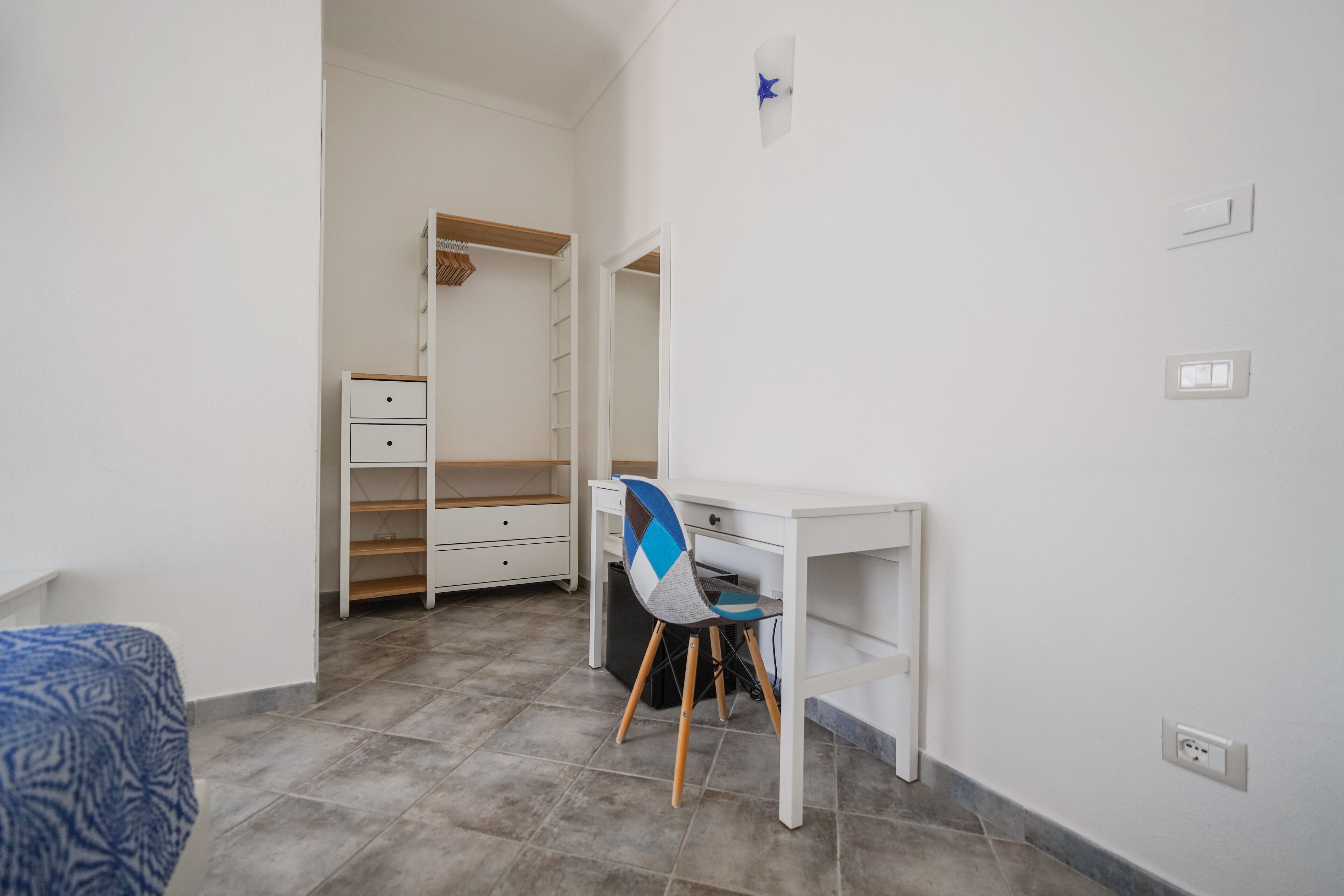 A room with a white desk, a chair, a wardrobe, and a bed.