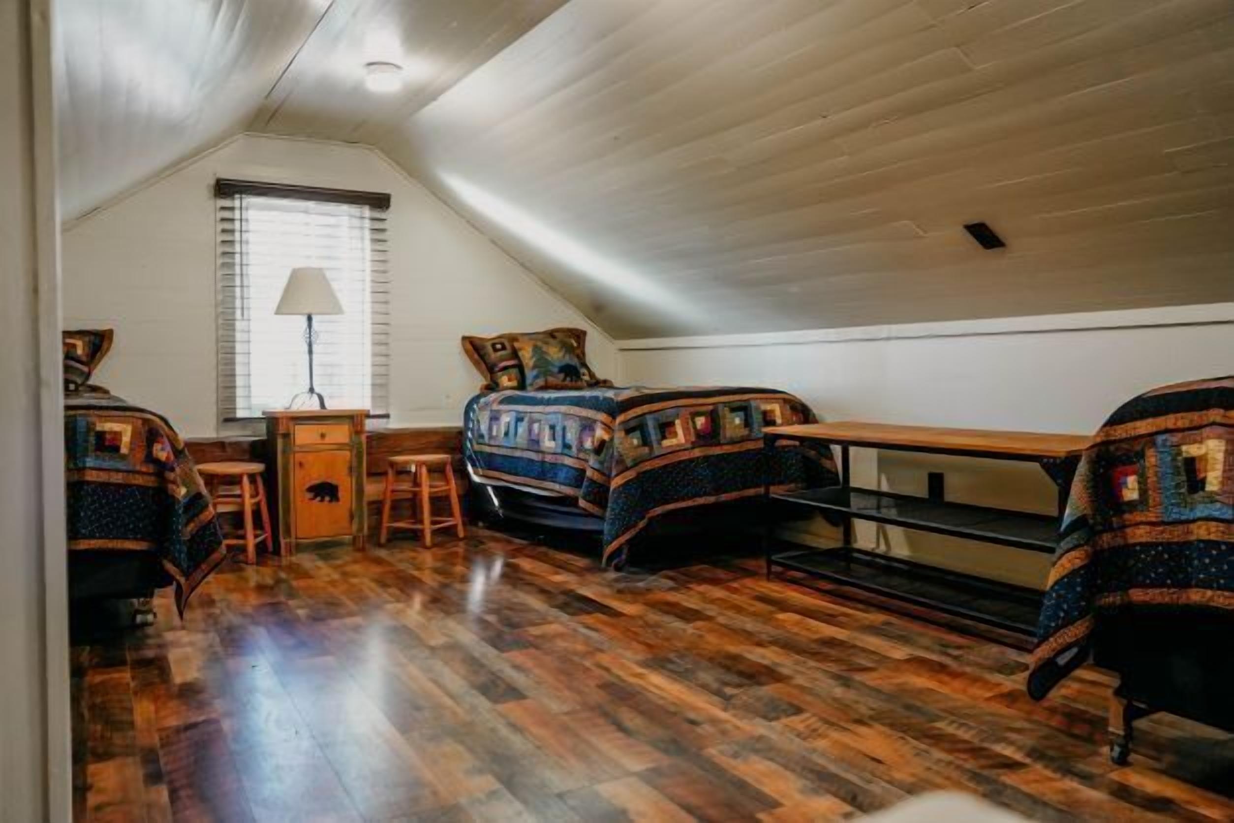 A cozy attic bedroom with wooden floors, a sloped ceiling, and a bed with a quilt.