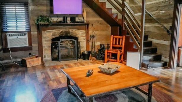 Una sala de estar acogedora con una chimenea de piedra, una mesa de madera y una escalera que sube a un nivel superior.