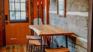Una mesa de madera con dos taburetes en un interior rústico, con una puerta y persianas de madera.