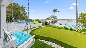 A pool area with a swing chair, lounge chairs, and a view of the water. - Aquarius South: Luxe 10BR/6BA , w/ heated swimming pool+spa, private dock & more (Stuart)