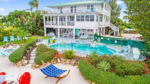 A two-story building with a swimming pool, surrounded by greenery and outdoor seating. - Aquarius South: Luxe 10BR/6BA , w/ heated swimming pool+spa, private dock & more (Stuart)