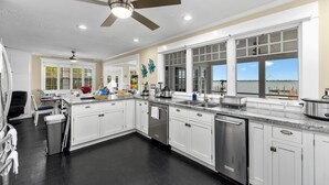 A modern kitchen with white cabinets, a granite countertop, and a view of the ocean through large windows. - Aquarius South: Luxe 10BR/6BA , w/ heated swimming pool+spa, private dock & more (Stuart)
