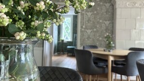 A dining area with a table and chairs, a vase with green foliage, and a patterned wall in the background. - Kinna Bed & Breakfast (Kinna)