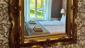 A bedroom with a large ornate mirror, a bed with pillows, a bedside table, and a hanging light fixture. - Kinna Bed & Breakfast (Kinna)
