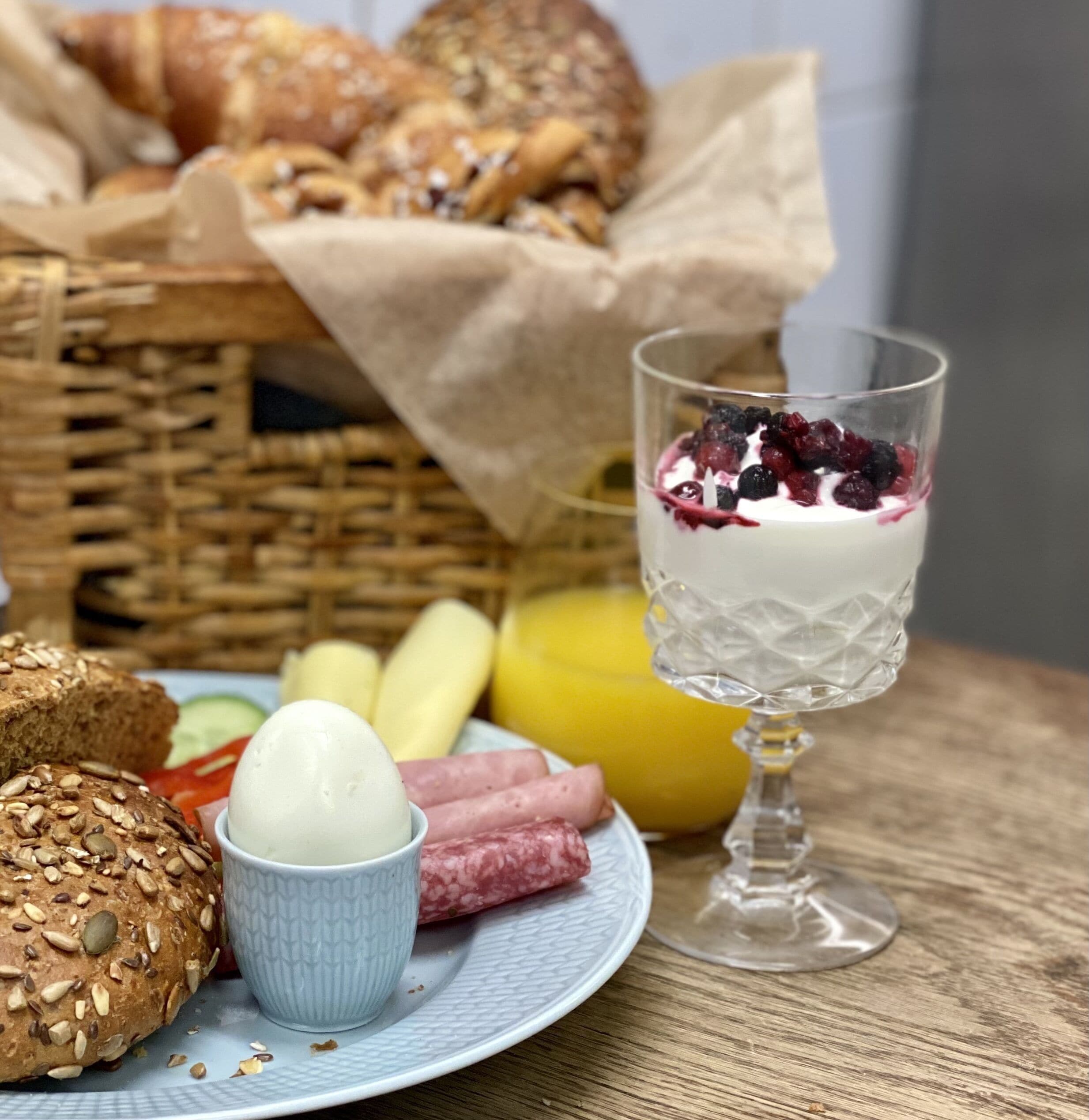 En morgenmadstallerken med brød, æg, skinke og et glas yoghurt toppet med bær.
