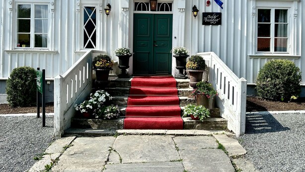 A white building with a green door, red carpeted stairs, and two flags. - Kinna Bed & Breakfast (Kinna)