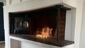 A fireplace with a brick surround and a white mantel, featuring a black wood-burning stove. - Kinna Bed & Breakfast (Kinna)