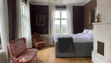 A bedroom with a bed, a chair, a table with candles, and a painting on the wall.